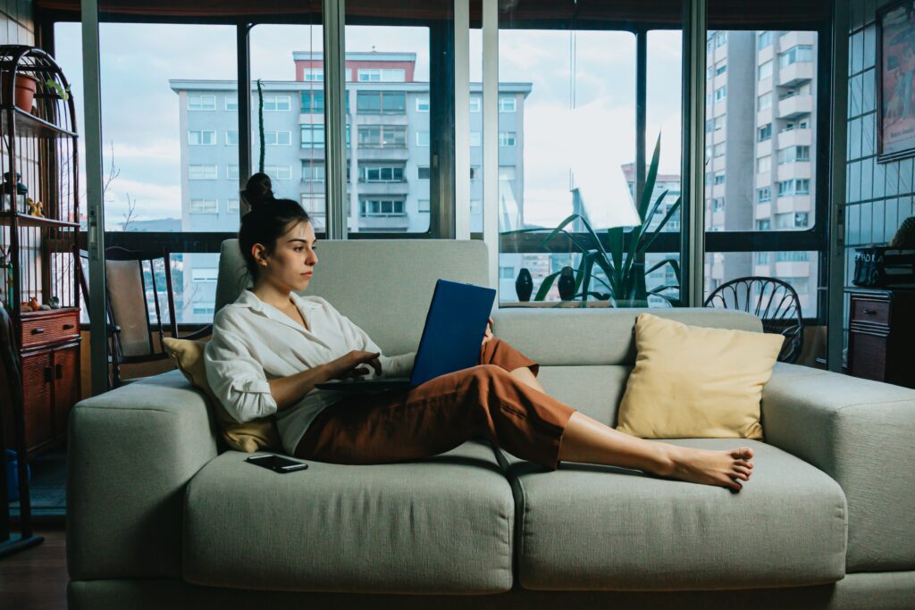 A woman sitting on a sofa while working on a laptop on her lap